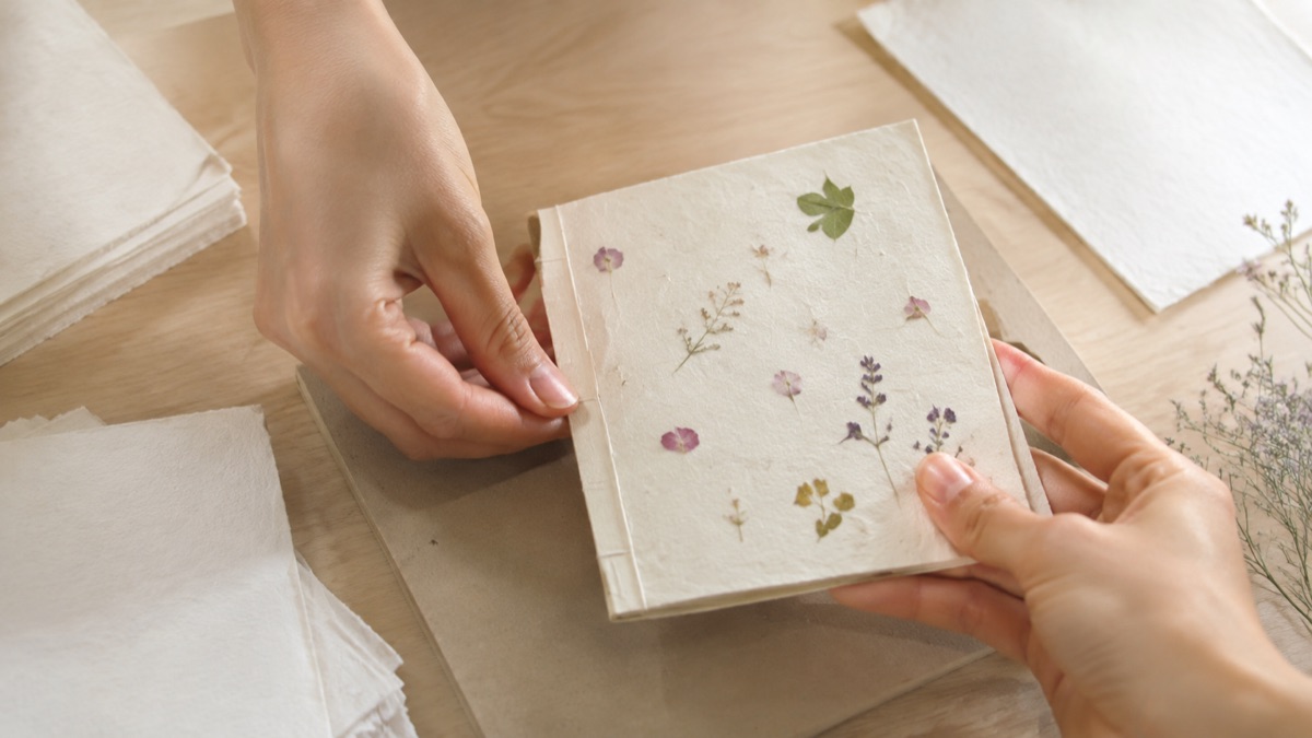 Hands assembling a blank washi journal with pressed flowers; illustrative scene